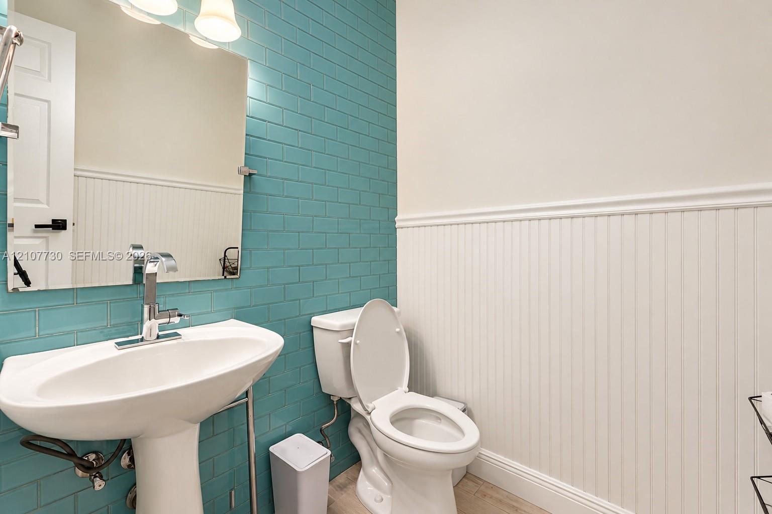 Bathroom featuring a pedestal sink with a chrome finish faucet, blue subway tile backsplash, white beadboard wainscoting, and a wall-mounted mirror