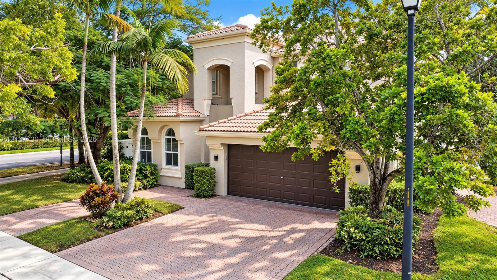 Stucco exterior featuring arched windows, a multi-tiered tile roof, and a paved driveway leading to an attached two-car garage