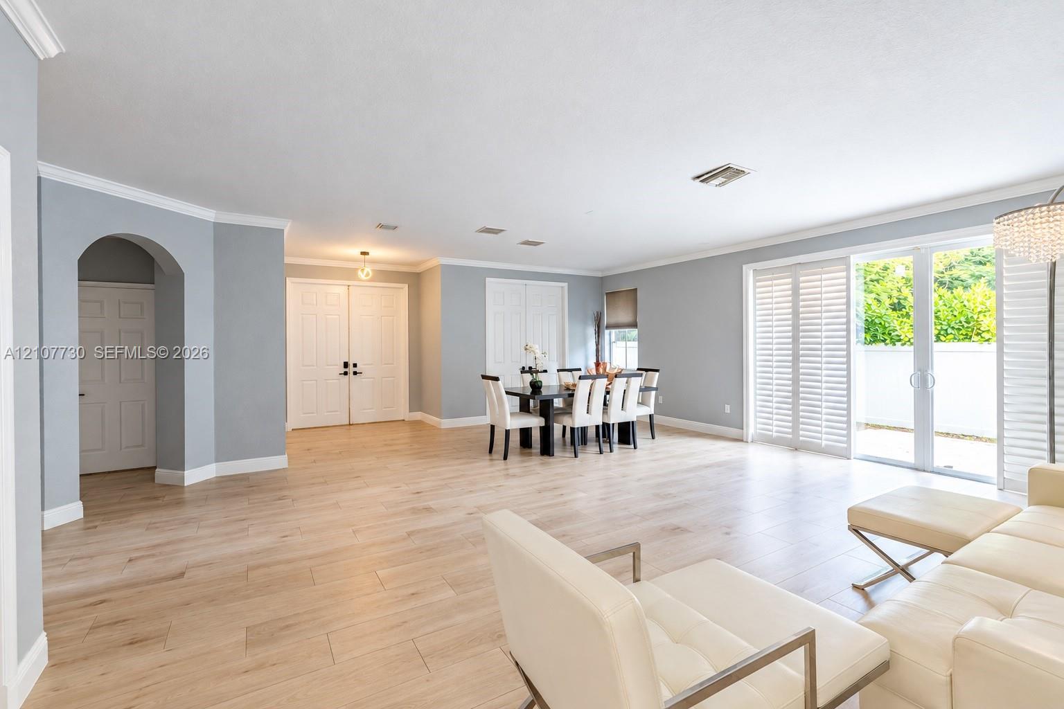 Open-concept living space featuring wood-finish flooring, crown molding, arched entryway, and multi-panel sliding glass doors with plantation shutters