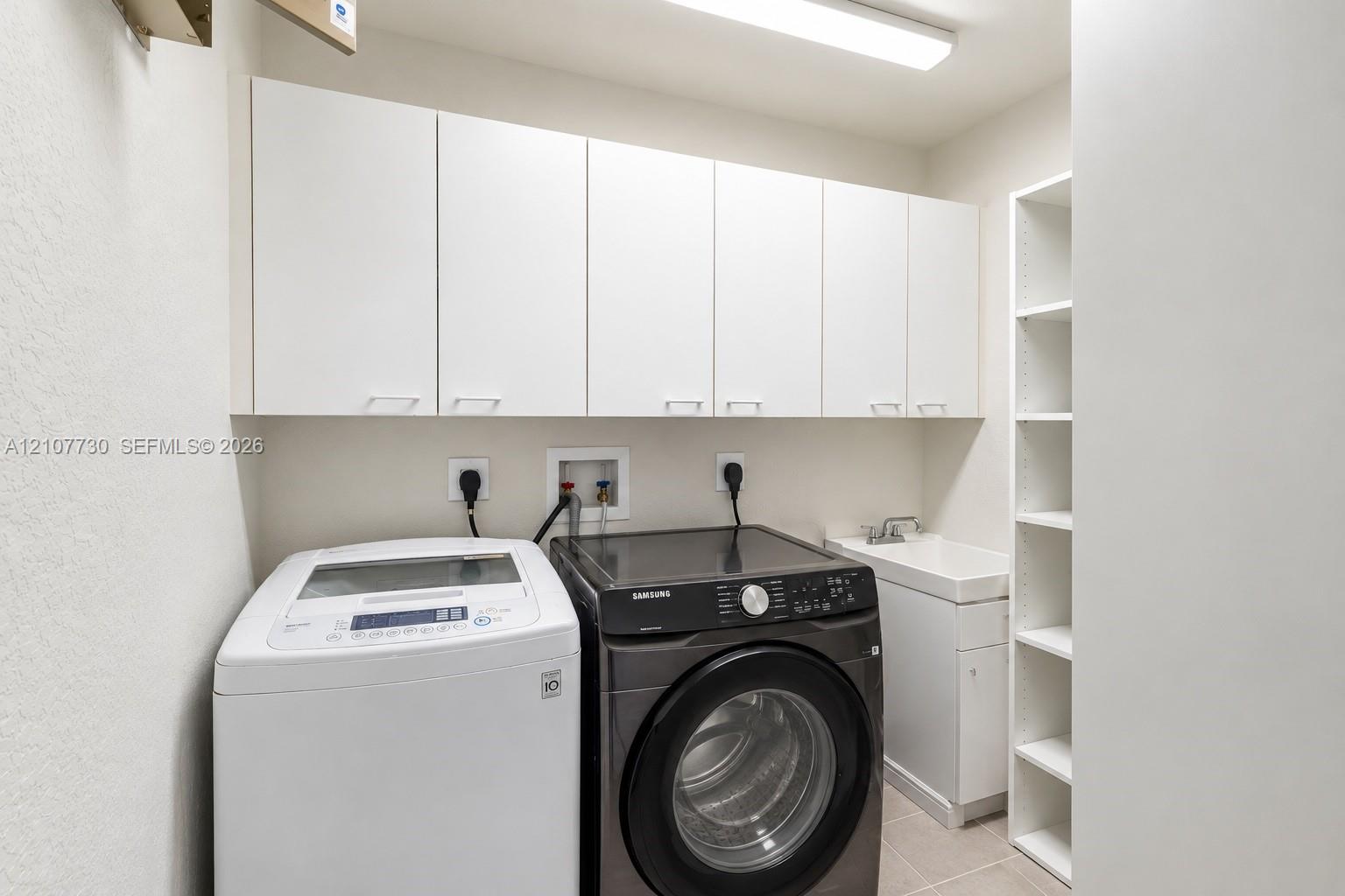 Laundry room featuring white wall-mounted cabinetry, integrated open shelving, a utility sink with white vanity base, and overhead lighting