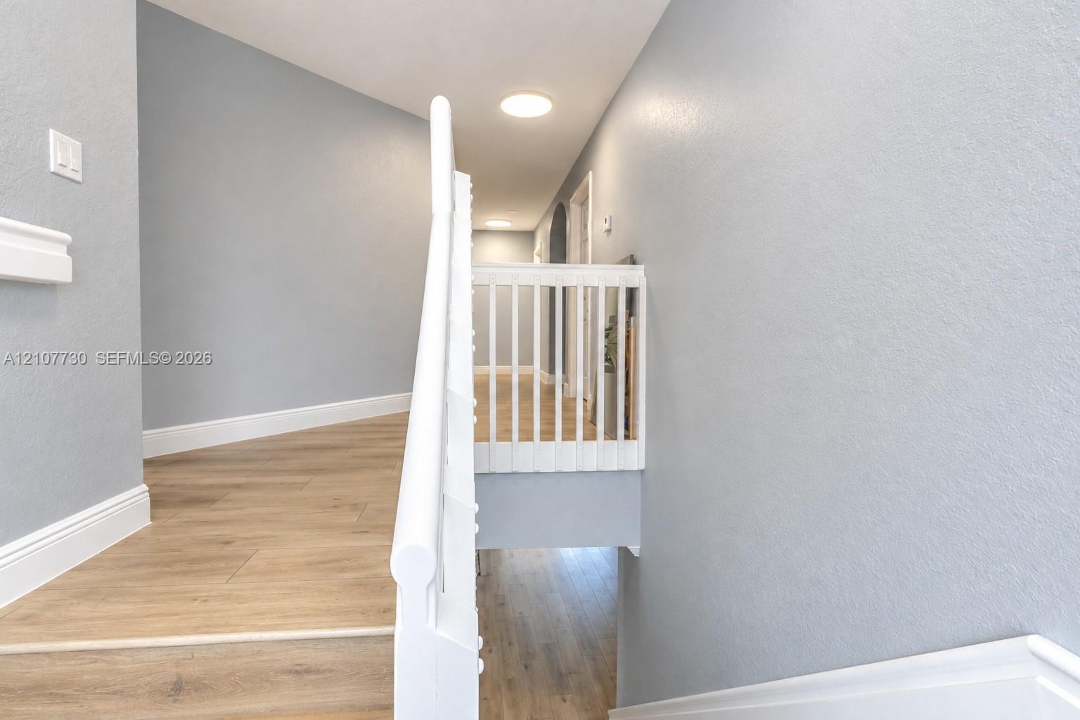 Hallway featuring wood-finish flooring, white spindle railing, recessed ceiling lighting, and neutral wall paint
