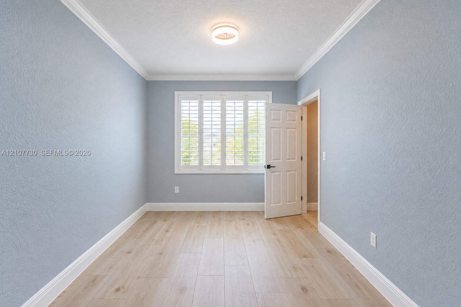 Light-filled interior featuring wood-finish flooring, plantation shutters, crown molding, and a neutral color palette