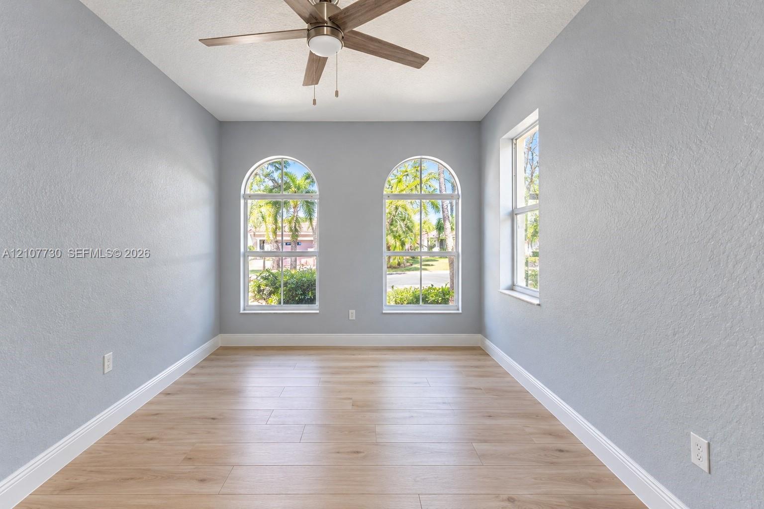 Room featuring wood-finish flooring, two arched windows, a single rectangular window, and a ceiling fan