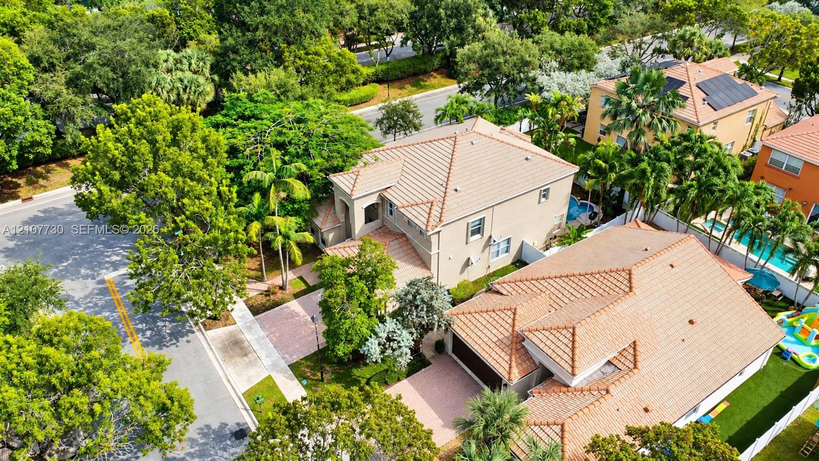 Aerial perspective of a multi-story residence featuring a clay tile roof, paved driveway, integrated garage, and mature landscaping