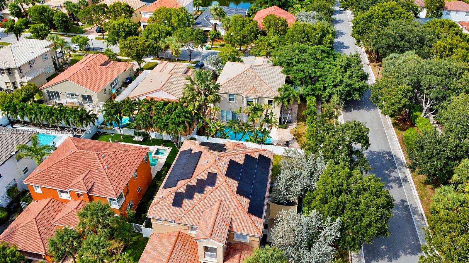 Aerial perspective featuring tile roofing, roof-mounted solar panels, private swimming pools, and mature landscaping