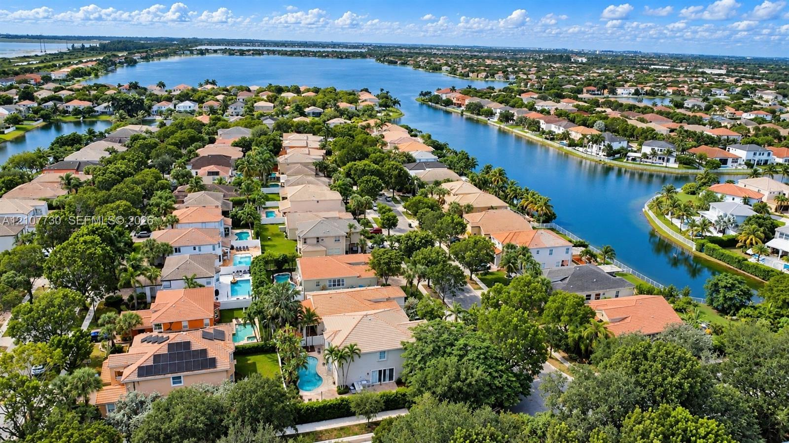 Aerial perspective of a residential neighborhood featuring waterfront positioning, tile roof architecture, backyard swimming pools, solar panel installations, and mature landscaping