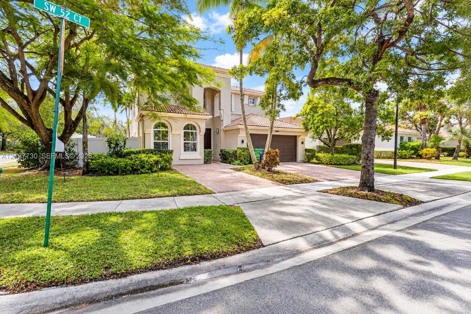 Two-story residence featuring a tile roof, arched windows, concrete paver driveway, and mature landscaping