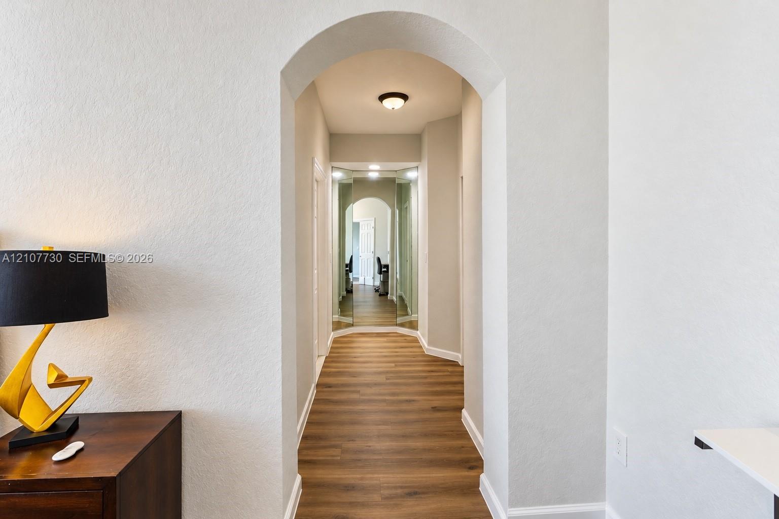Arched doorway featuring wood-finish flooring, neutral wall paint, and mirrored wall panels
