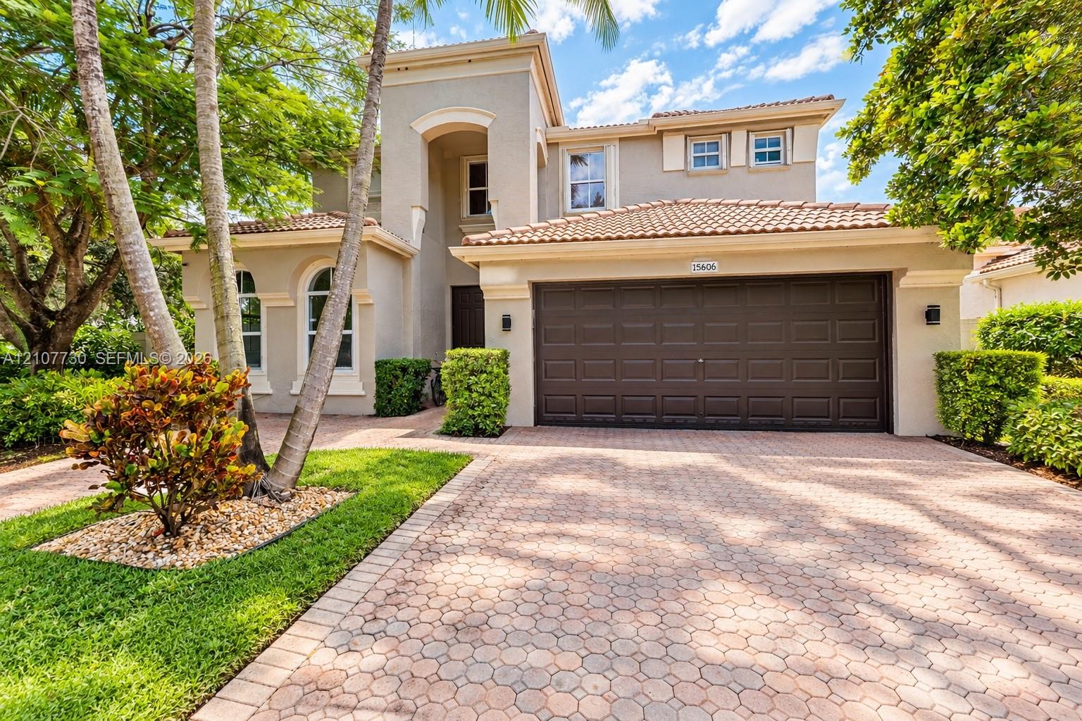 Two-story residence featuring a tile roof, stucco exterior, multi-pane arched windows, and a paved stone driveway with an attached two-car garage