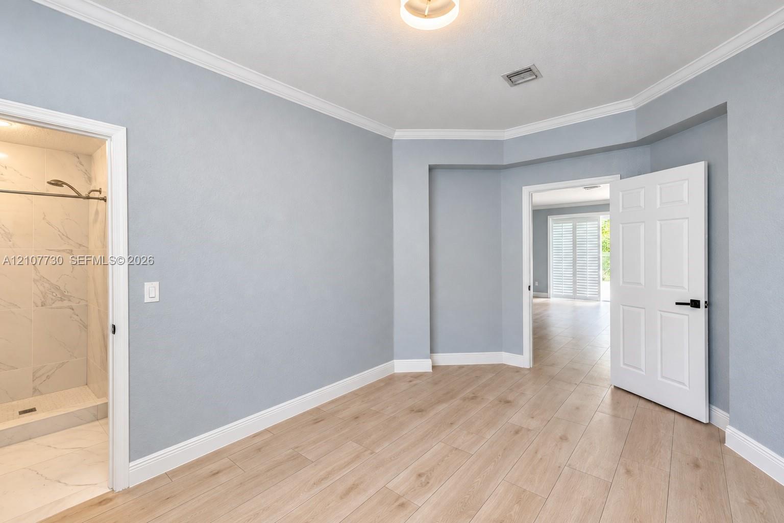 Room featuring wood-finish tile flooring, crown molding, multi-panel doors with matte black hardware, and an en-suite with stone-finish wall tile and a walk-in shower
