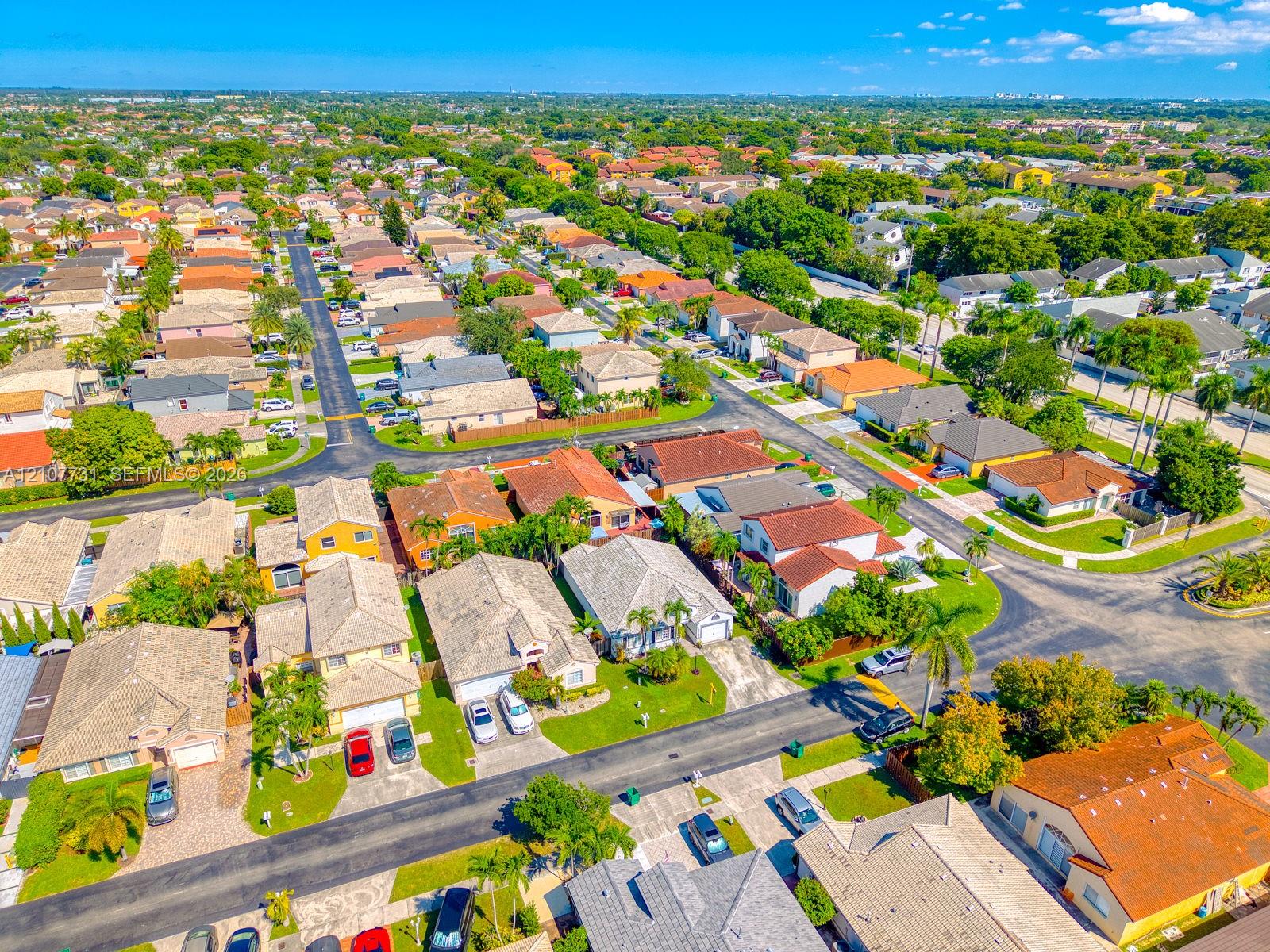 Aerial perspective of a suburban neighborhood featuring paved street grids, detached single-family residences with pitched rooflines, concrete driveways, and established landscaping with palm trees
