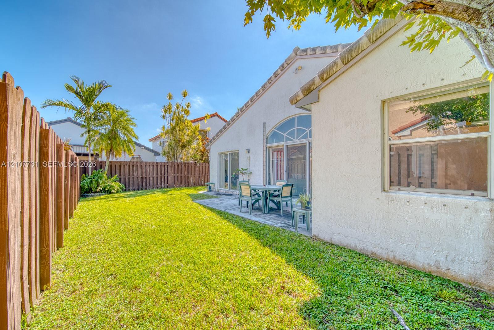 Stucco exterior featuring a paved rear patio, arched window detailing, and a privacy wood-slat fence enclosing the backyard