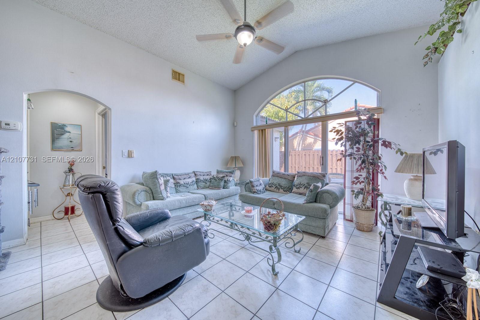 Vaulted ceilings, arched window, sliding glass door, and neutral ceramic tile flooring