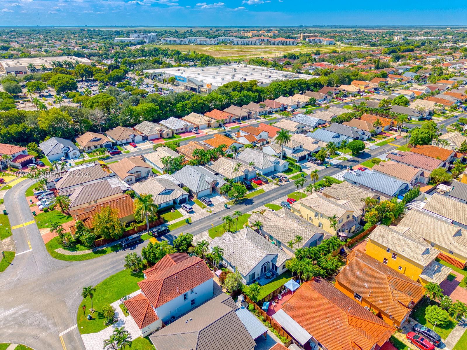 Aerial perspective of a residential neighborhood featuring diverse rooflines, established mature trees, manicured lawns, and paved street infrastructure