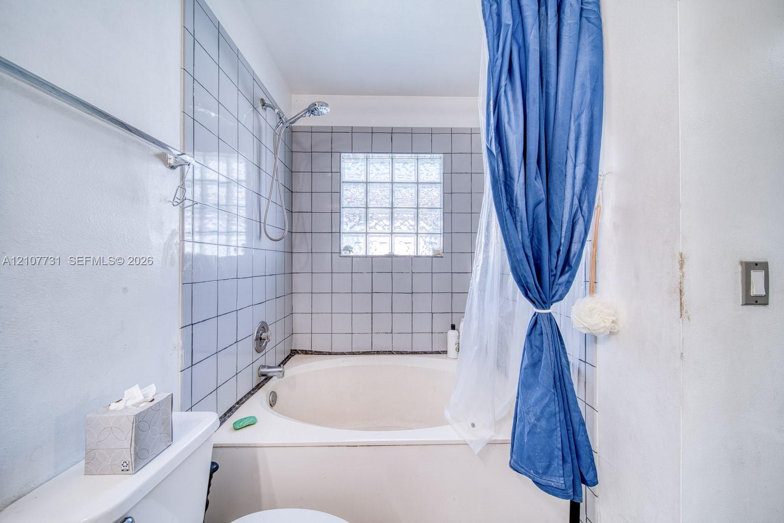 Deep soaking tub with a tiled surround, integrated shower fixture, and a glass block window
