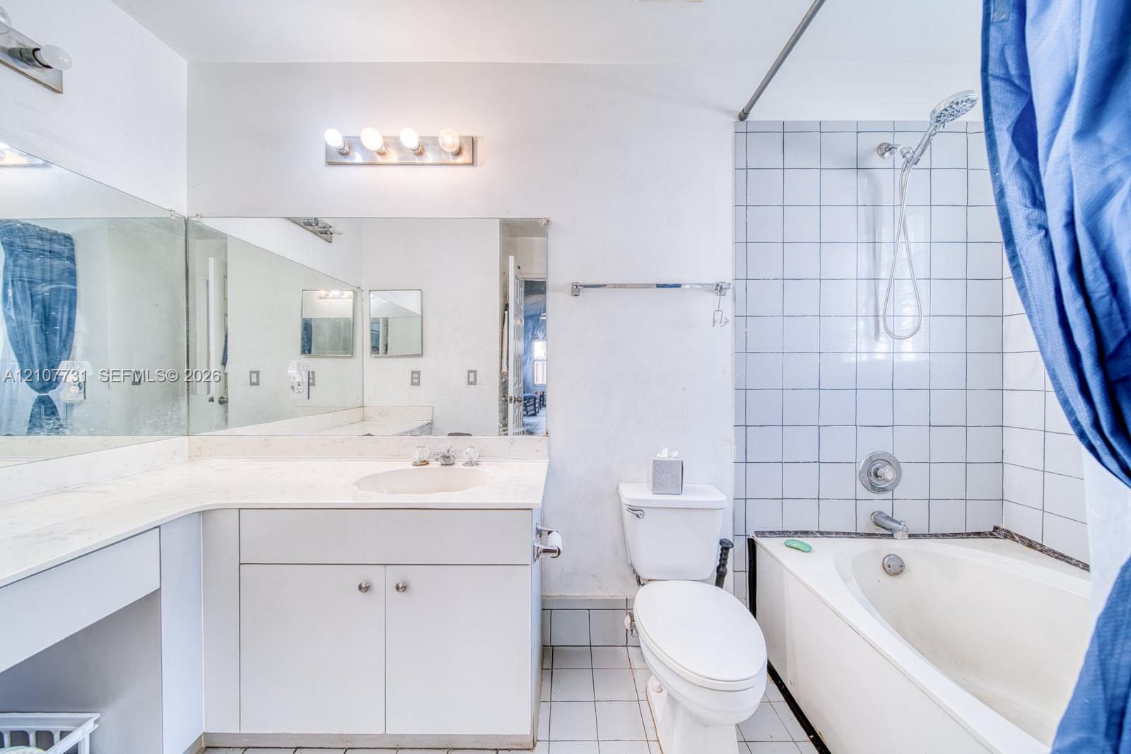 Bathroom featuring a vanity with a white countertop and integrated sink, a full-width wall mirror, a bathtub-shower combination with white wall tile, and built-in cabinetry