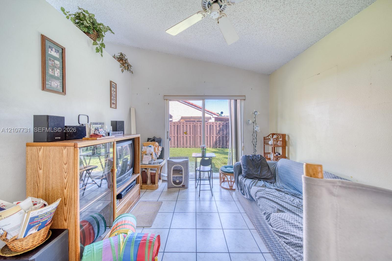 Living area featuring tile flooring, vaulted ceilings, a ceiling fan, and sliding glass doors providing outdoor access