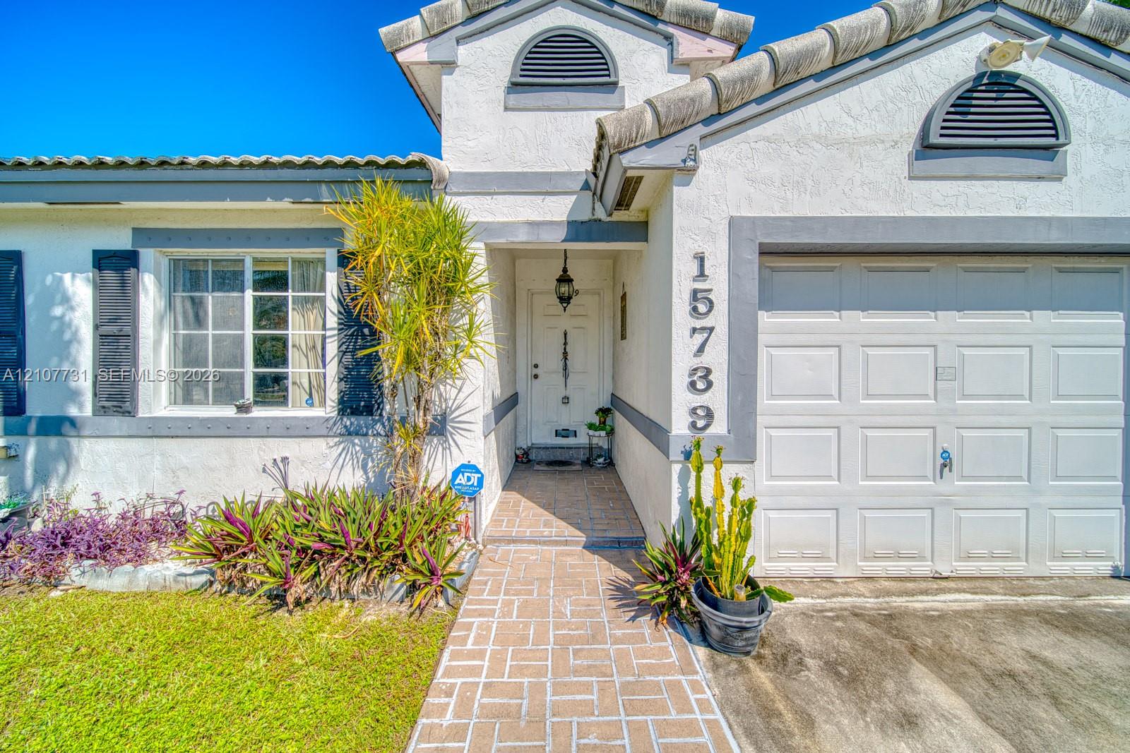 Stucco exterior featuring arched gable vents, a paved walkway, and a single-car garage with a paneled door