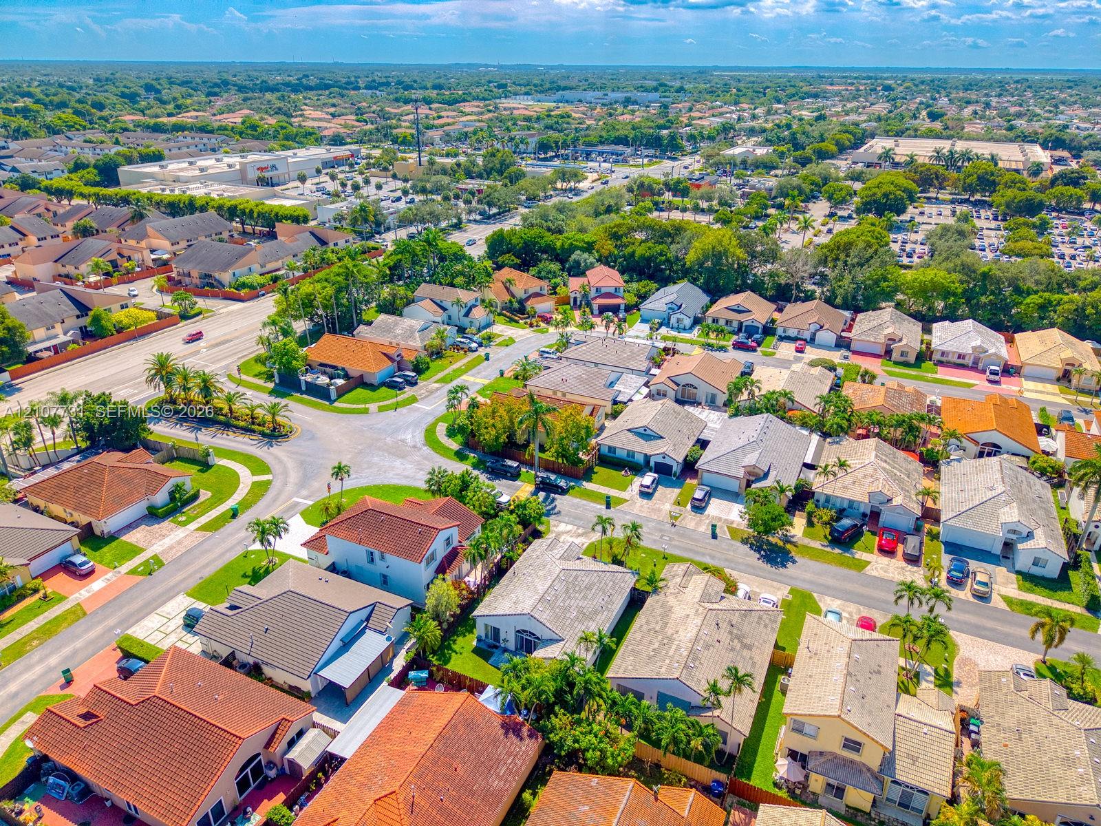 Aerial perspective of a suburban neighborhood featuring residential homes with tile roofing, paved streets, and mature landscaping