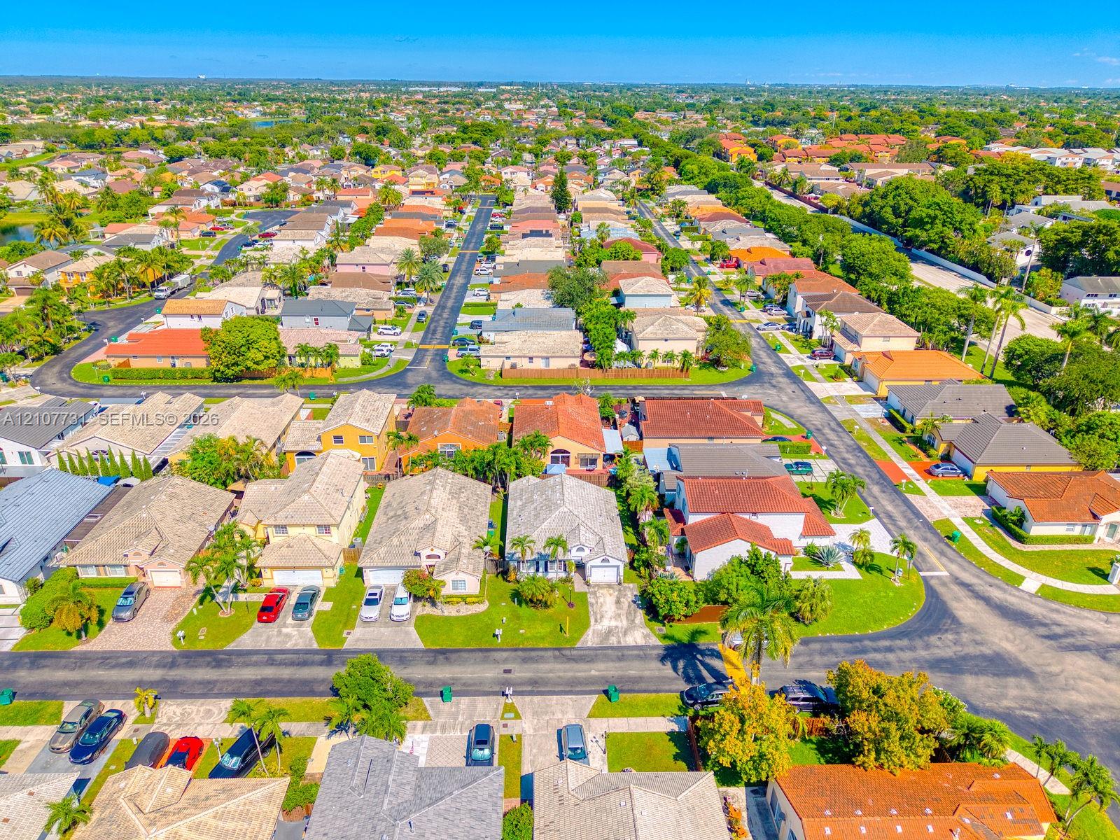 Aerial perspective of a suburban neighborhood featuring paved streets, mature landscaping, and residential homes with tiled roofing