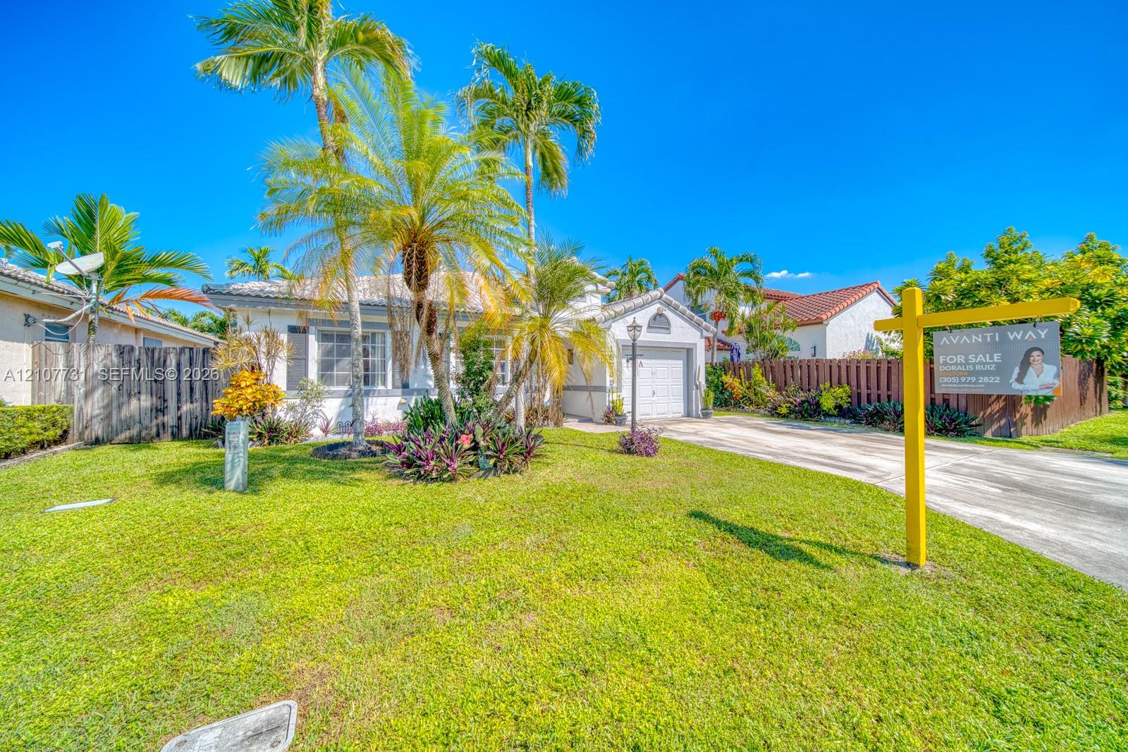 Single-story residence featuring a tile roof, light-toned stucco exterior, integrated garage, and landscaped front yard with mature palm trees