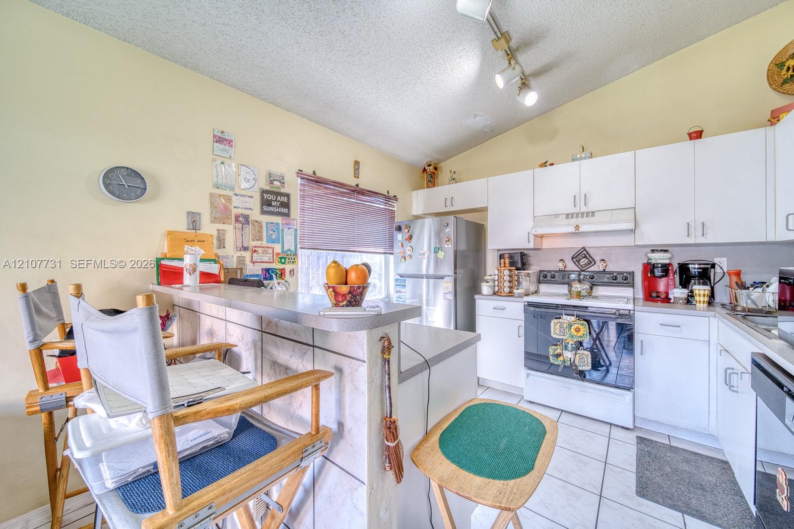 Kitchen featuring white cabinetry, solid-surface countertops, tile flooring, vaulted ceiling, and adjustable track lighting