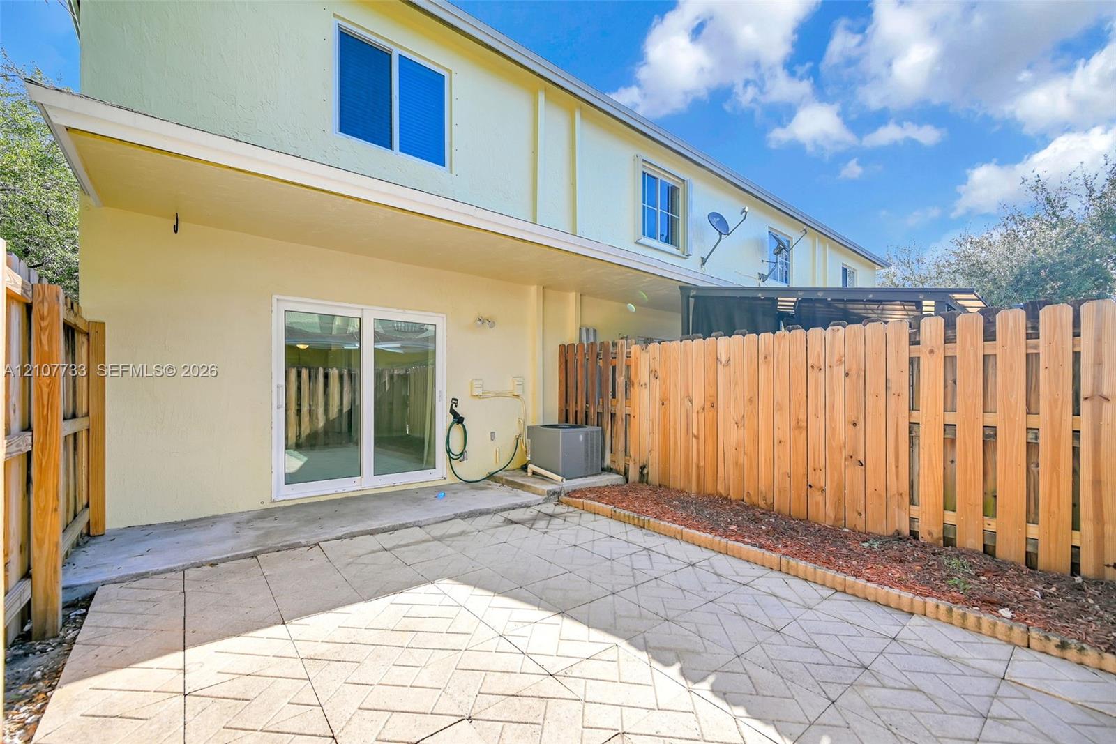 Rear patio featuring patterned paver hardscaping, dual-panel sliding glass doors, and a wood privacy fence