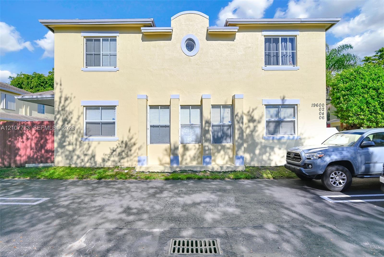Two-story exterior featuring a stucco finish, rhythmic vertical columns, an arched roofline parapet, a central oval window, and grid-patterned windows