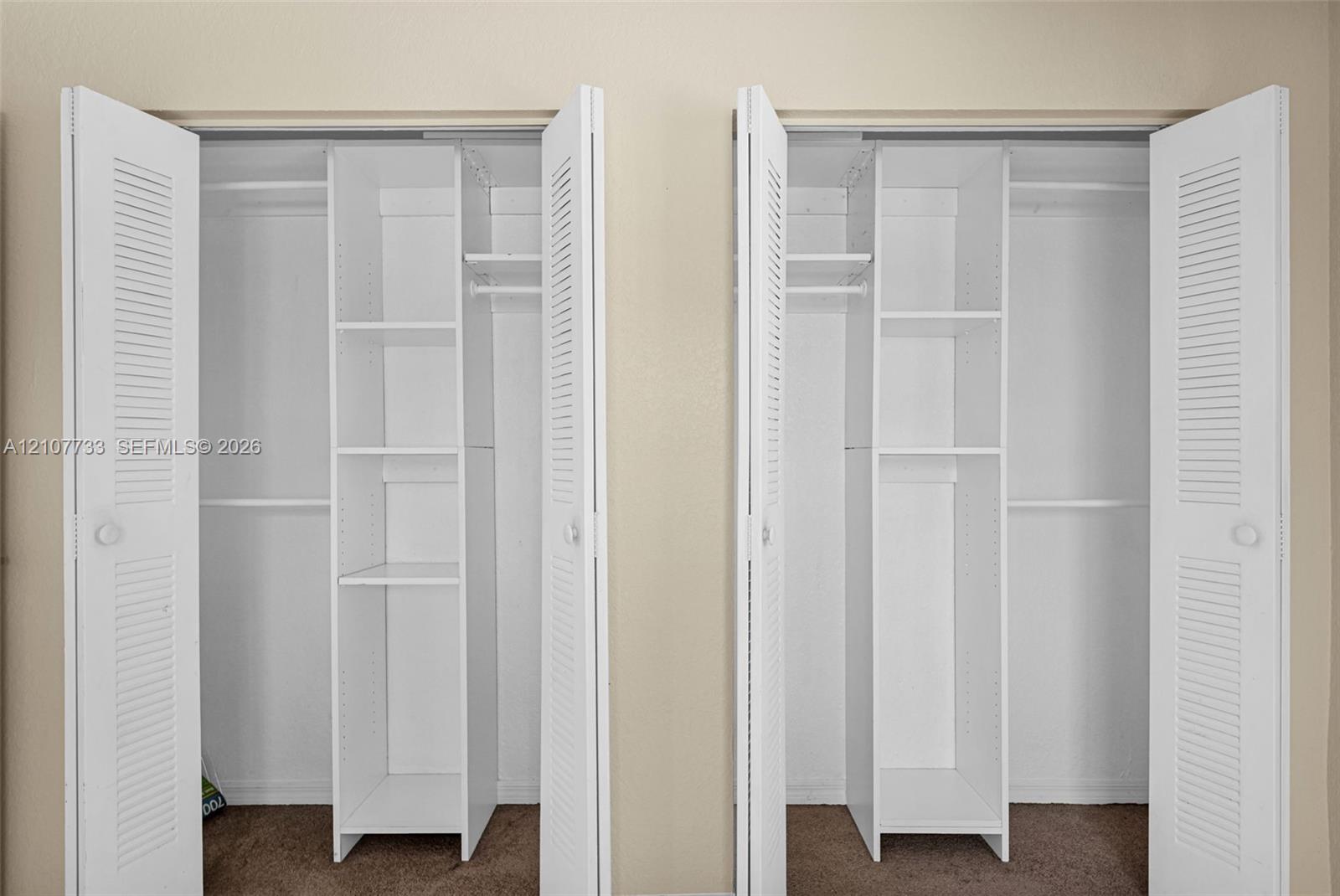 Dual closets featuring white louvered doors, built-in shelving towers, and integrated hanging rods