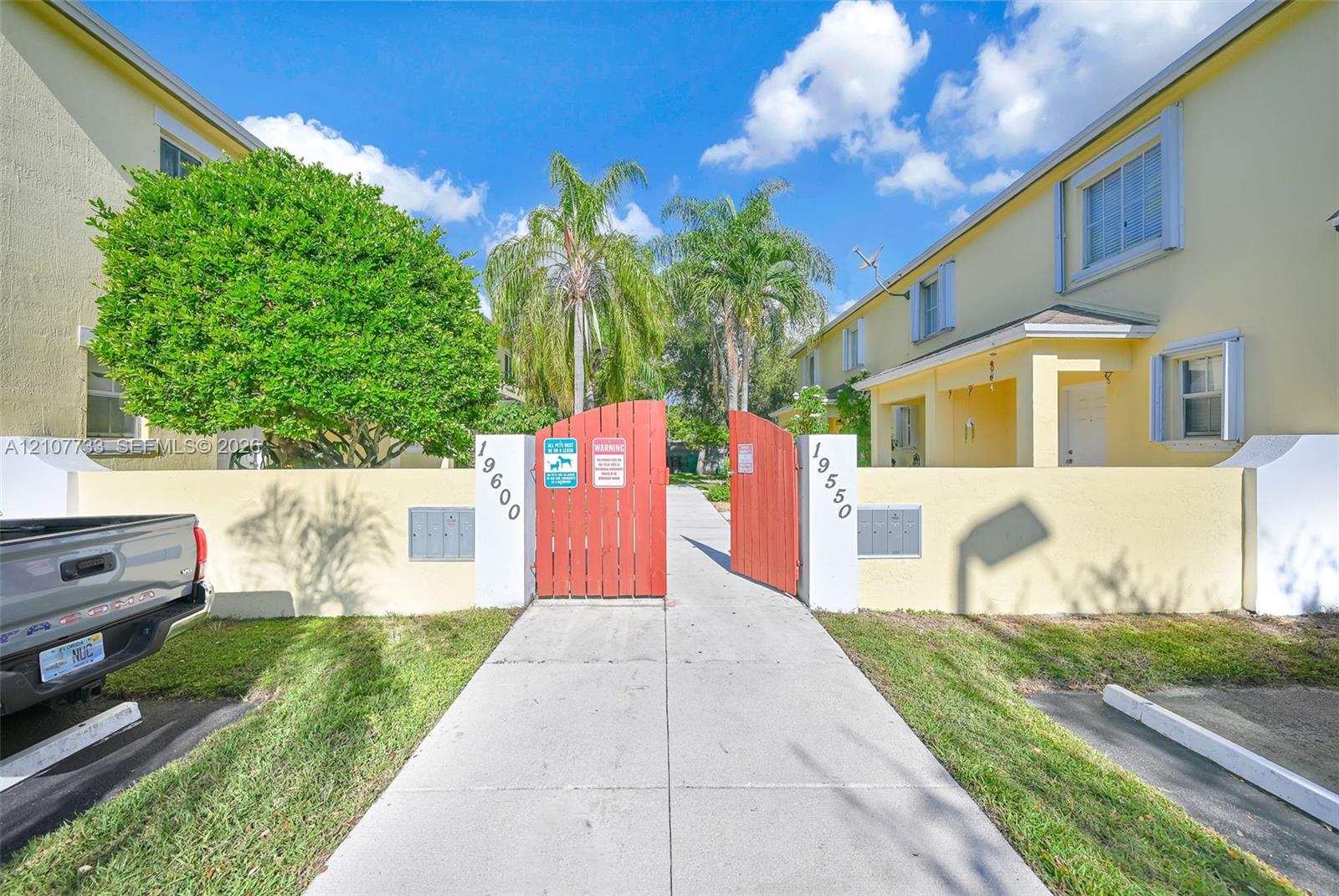 Stucco exterior buildings with a gated entry, concrete walkway, and palm tree landscaping