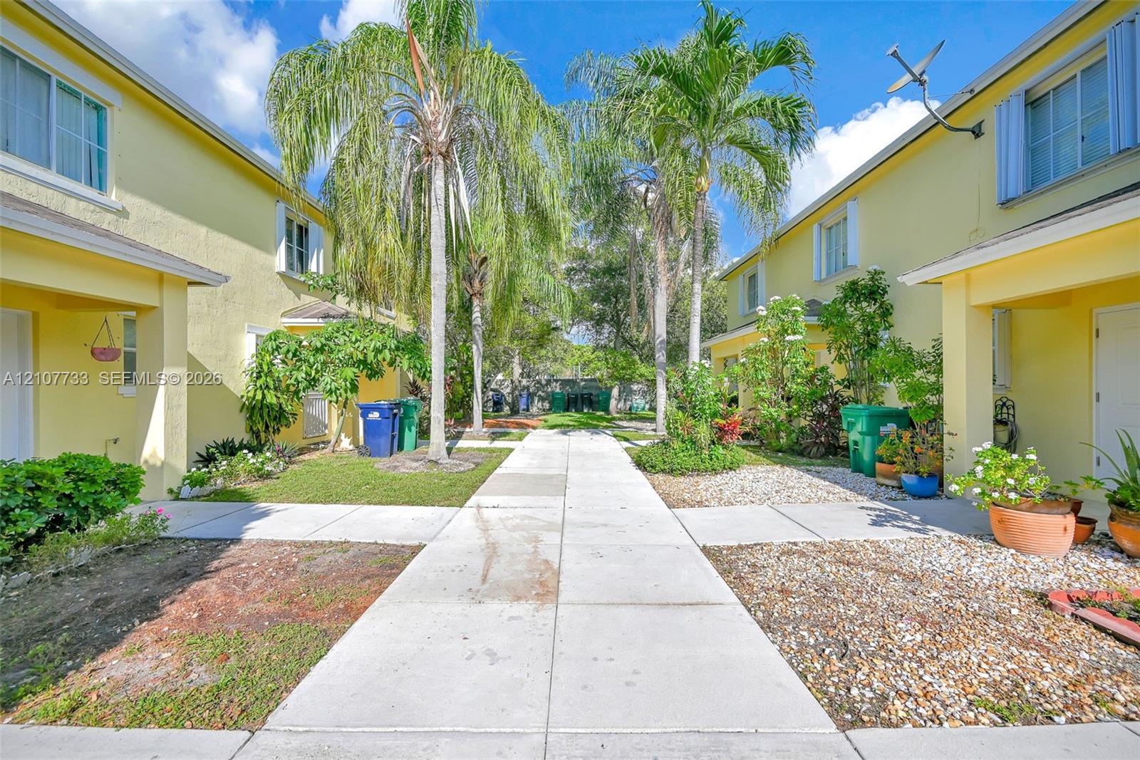 Stucco exterior with multi-story facades, concrete walkway, and mature palm landscaping