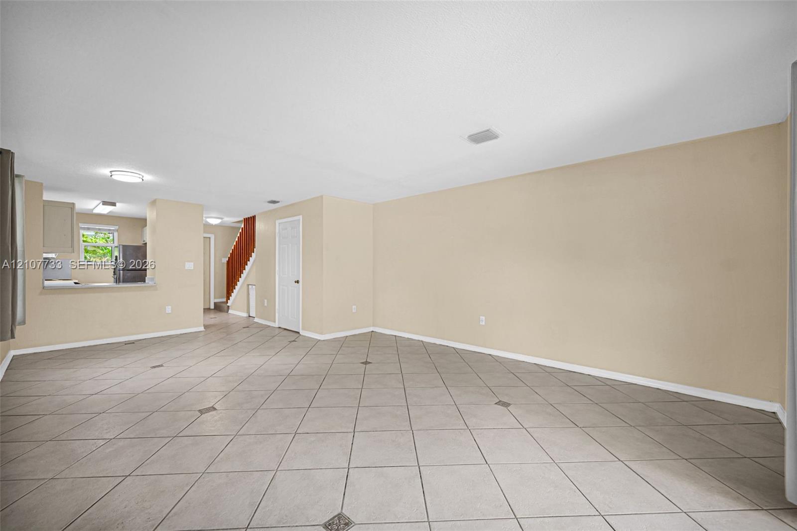 Open-concept interior featuring large-format diagonal tile flooring with decorative inlay accents, neutral wall tones, recessed ceiling lighting, and a built-in staircase with a wood-finish handrail