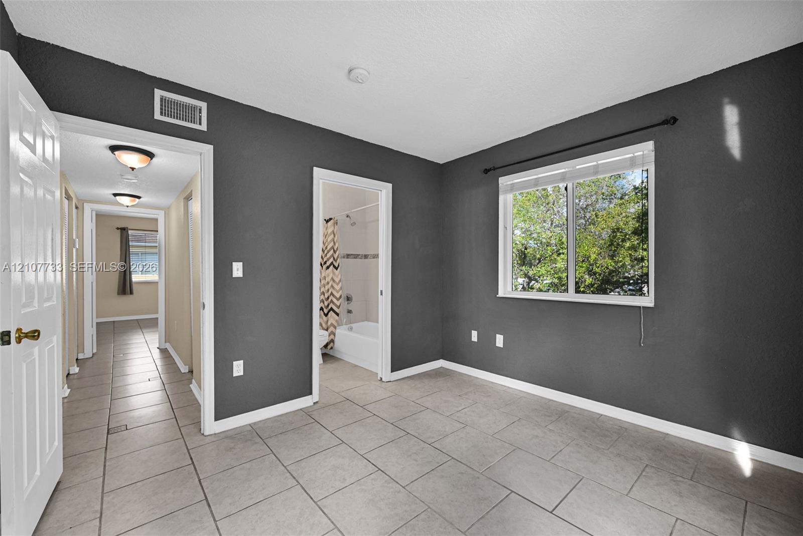 Room featuring large-format ceramic tile flooring, a single-pane window with white trim, and neutral wall tones