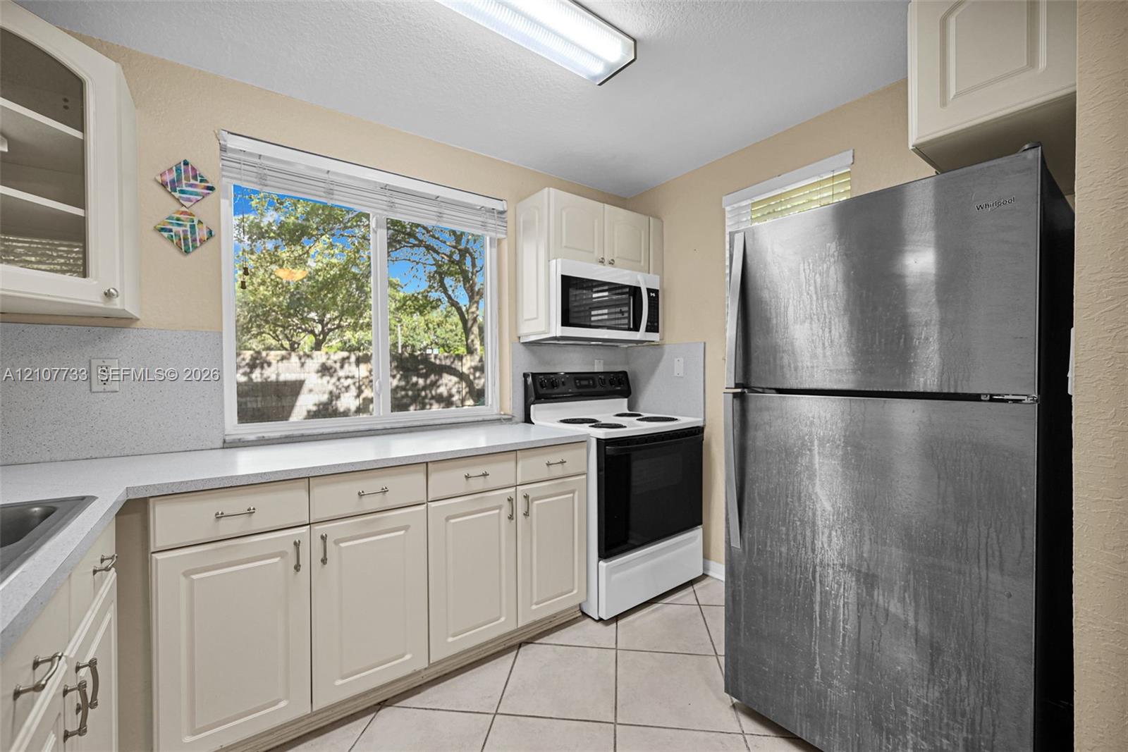 Kitchen featuring off-white cabinetry, solid surface countertops, a stainless steel refrigerator, white electric range, and tile flooring