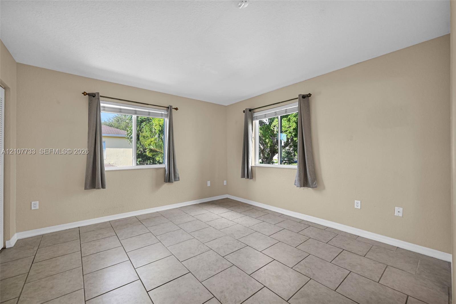 Neutral-toned interior featuring large-format ceramic tile flooring, dual windows with double-track hardware, and textured ceiling finish