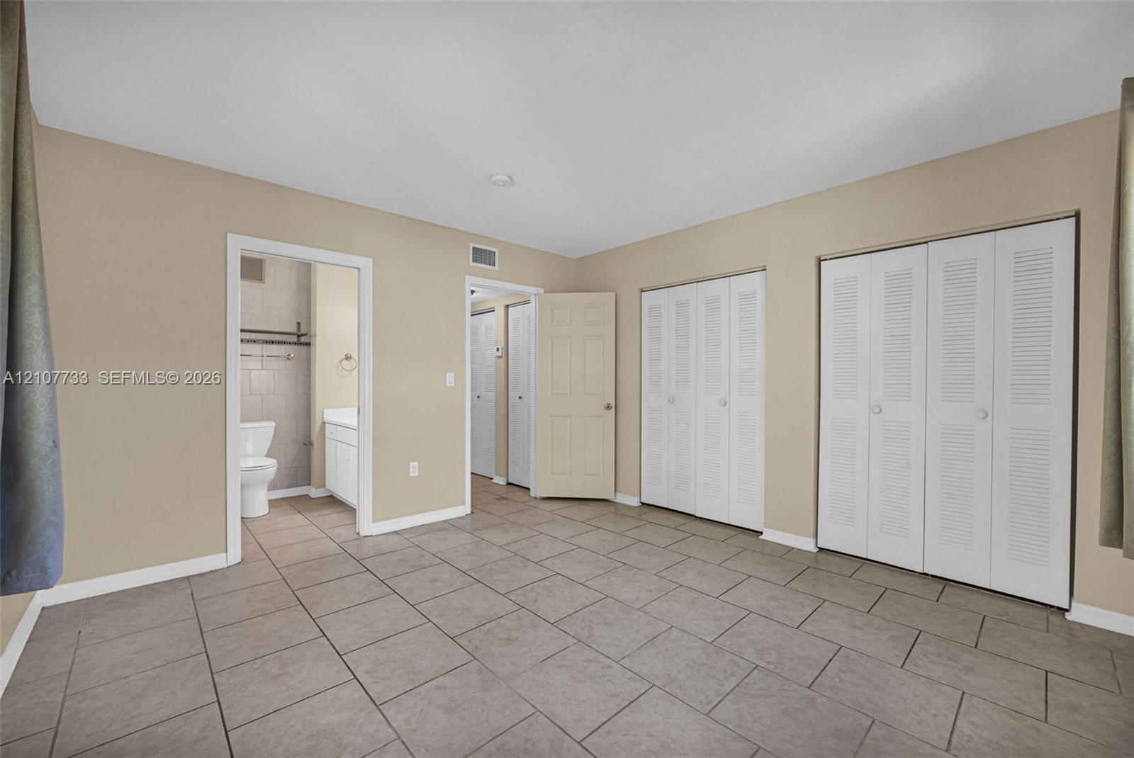 Tile flooring throughout, dual closets with louvered doors, and a bathroom featuring a vanity cabinet