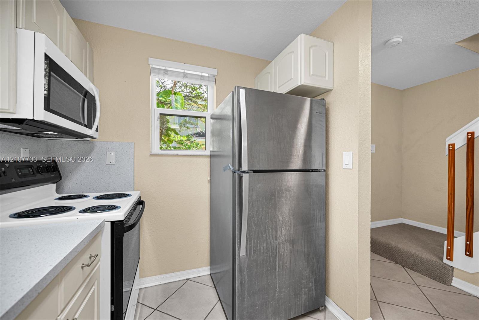Kitchen featuring white cabinetry, solid-surface countertops, stainless steel refrigerator, white electric range, and ceramic tile flooring