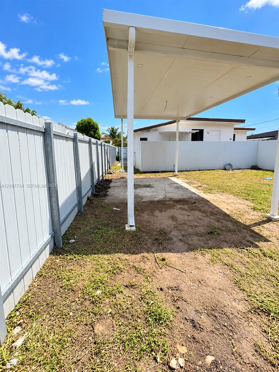 Covered patio featuring a concrete slab and white metal support posts, enclosed by a white vinyl perimeter fence Covered patio featuring a concrete slab and white metal support posts, enclosed by a white vinyl perimeter fence