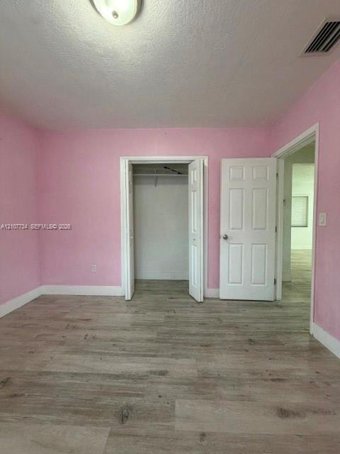 Wood-finish flooring, six-panel interior door, and closet featuring overhead storage shelving and a hanging rod