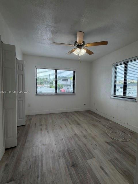 Interior room featuring wood-finish flooring, two dual-pane windows with horizontal blinds, a ceiling fan with integrated lighting, and a bi-fold closet door