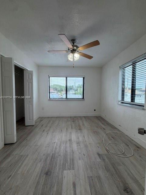 Room featuring wood-finish flooring, a ceiling fan with integrated lighting, dual windows with horizontal blinds, and a double-door closet