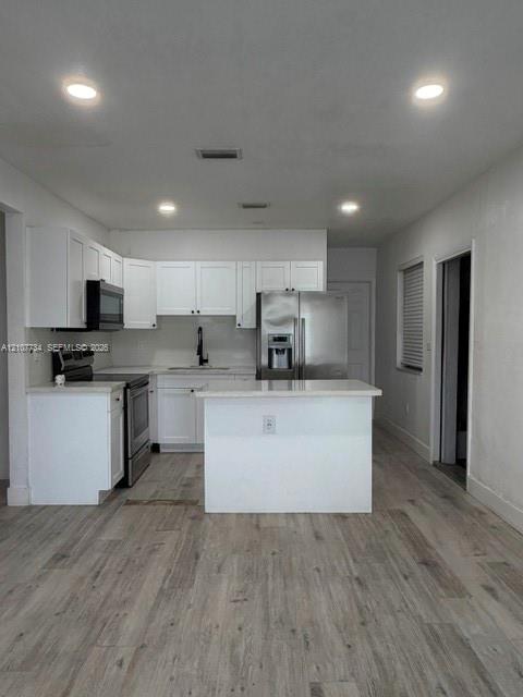Kitchen featuring white cabinetry, quartz countertops, a central island, stainless steel appliances, and wood-finish flooring
