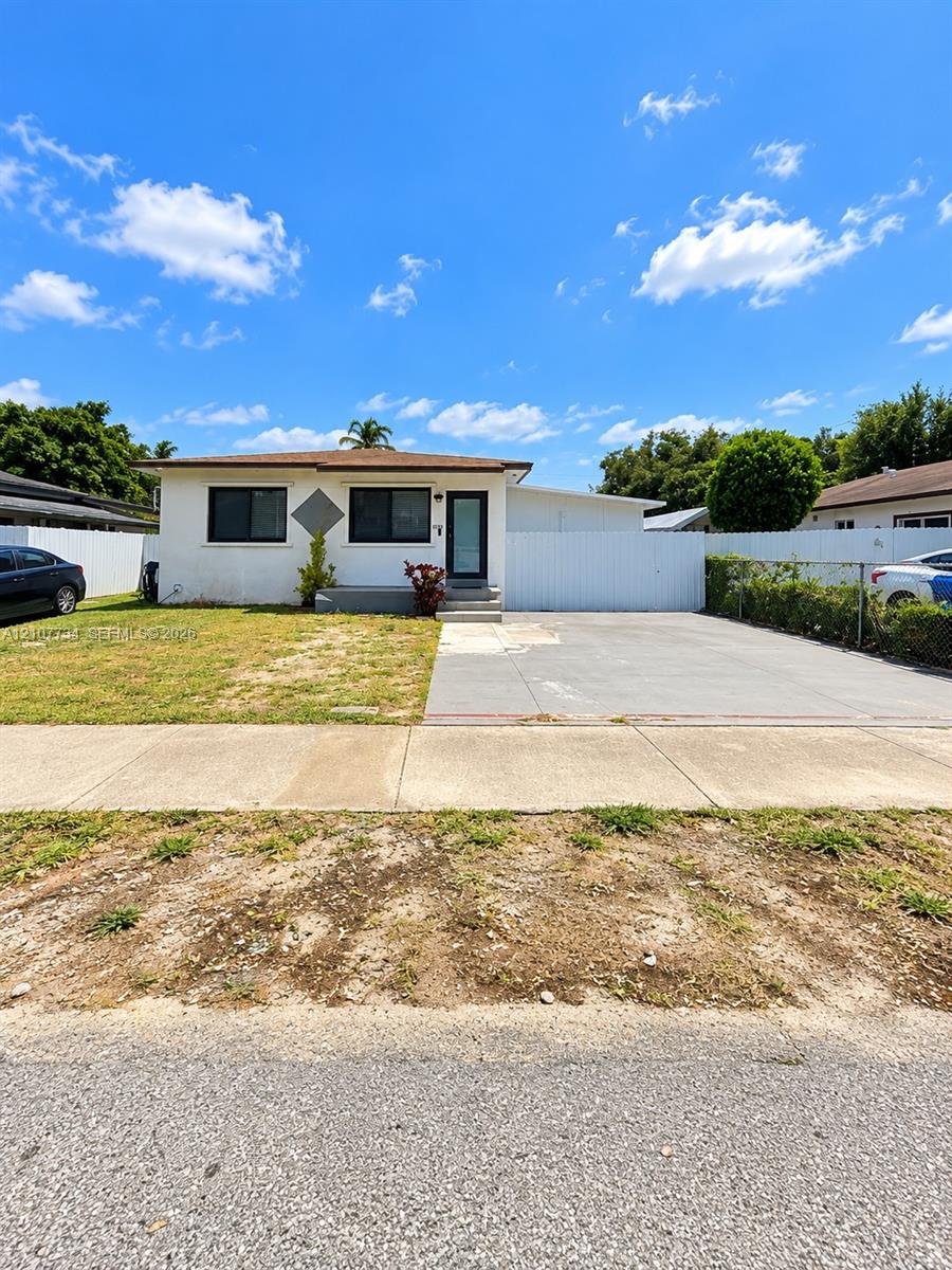 Single-story exterior featuring a light-toned stucco facade, concrete driveway, and full perimeter white fencing