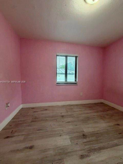 Room featuring wood-finish flooring, a central window with fitted horizontal blinds, and ceiling-mounted lighting