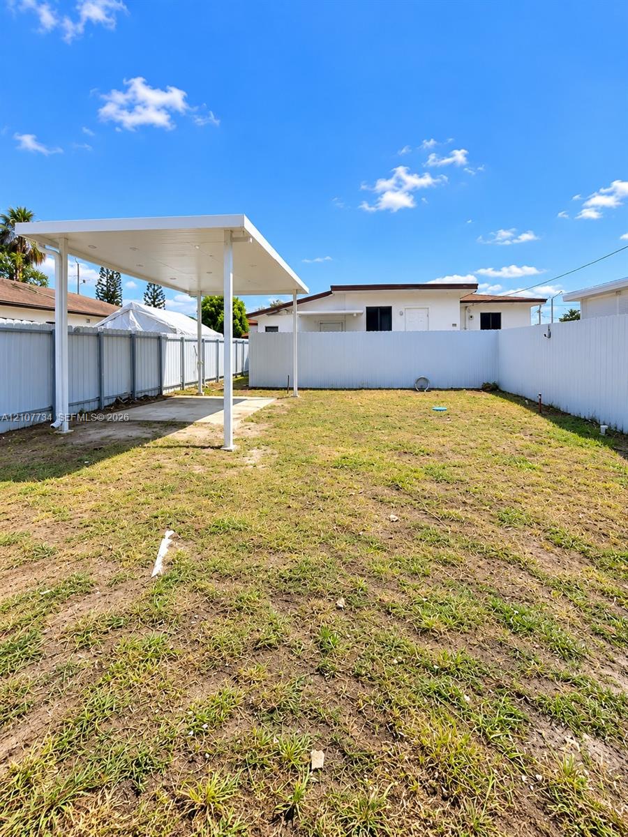 Fenced backyard featuring an expansive open lawn and a covered structural canopy with a concrete pad Fenced backyard featuring an expansive open lawn and a covered structural canopy with a concrete pad