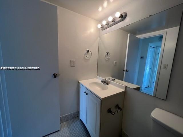 White vanity with an integrated sink and countertop, large wall-mounted mirror, four-light vanity fixture, and tiled flooring