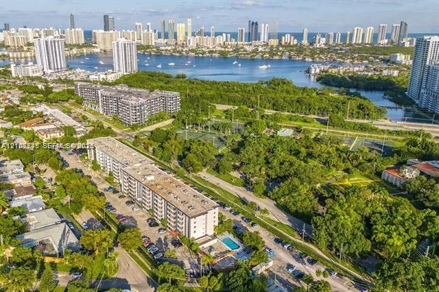 Aerial perspective featuring a multi-story residential building, an on-site swimming pool, paved surface parking, and proximity to expansive green space and coastal waterways