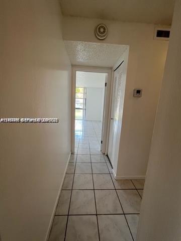 Hallway featuring light-colored tile flooring and a built-in closet with louvered doors