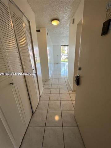 Hallway featuring white ceramic tile flooring, built-in louvered-door closets, and flush-mount lighting