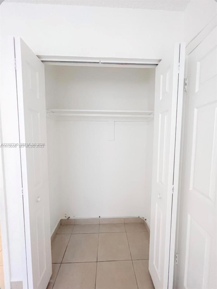 Reach-in closet featuring white paneled double doors, neutral tile flooring, and an integrated wire shelving unit